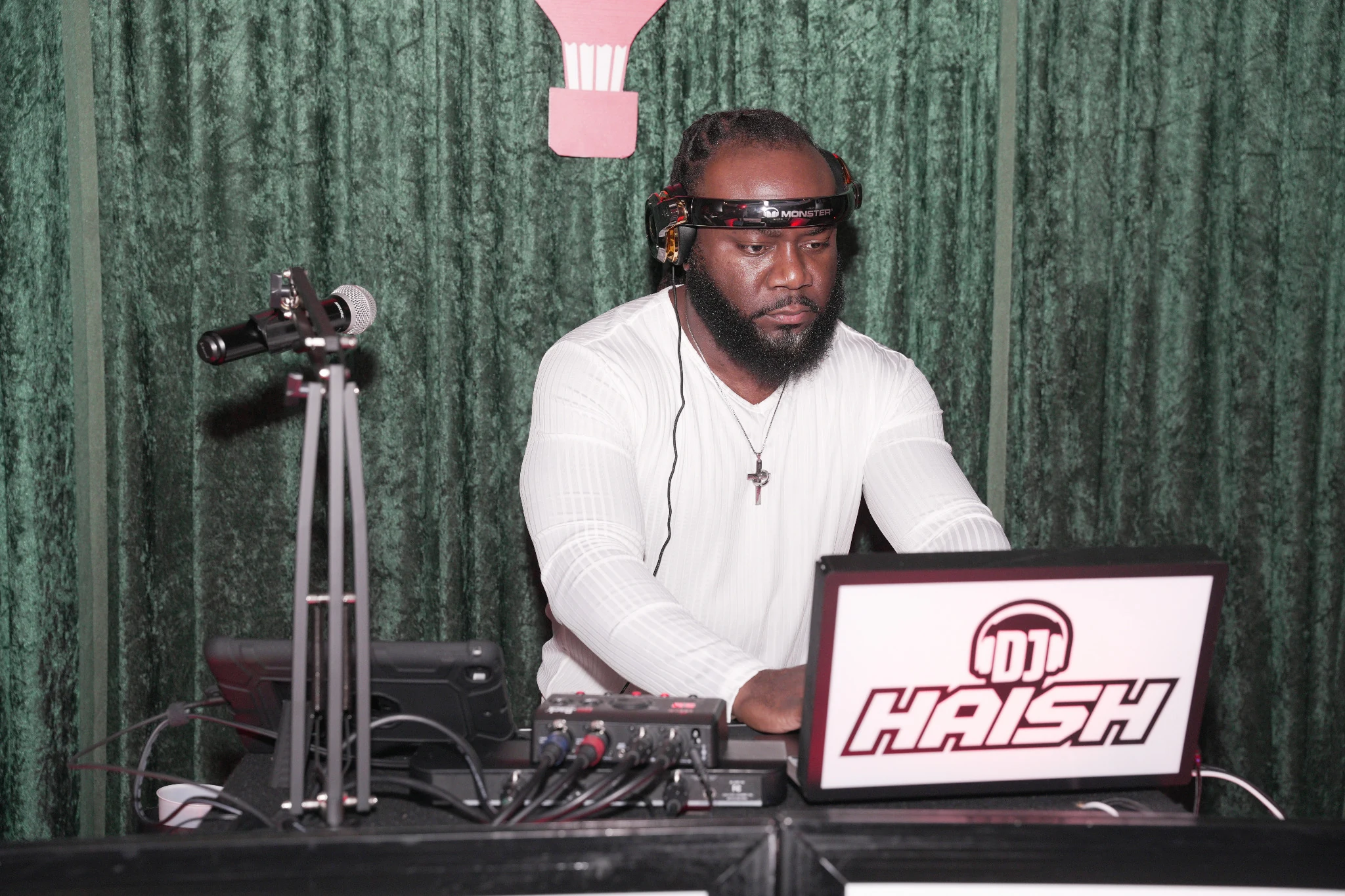 DJ Haish performing in a white shirt behind his branded DJ booth